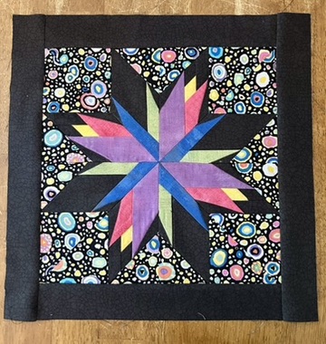 IDAHO STAR textile work by Michele Urbany Neely Puluti with a multicolored pointed star, black geometric wedges, and a lively circular-print background