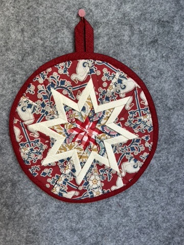 Round Scrappy Potholder with a layered cream star on red and navy patterned fabric