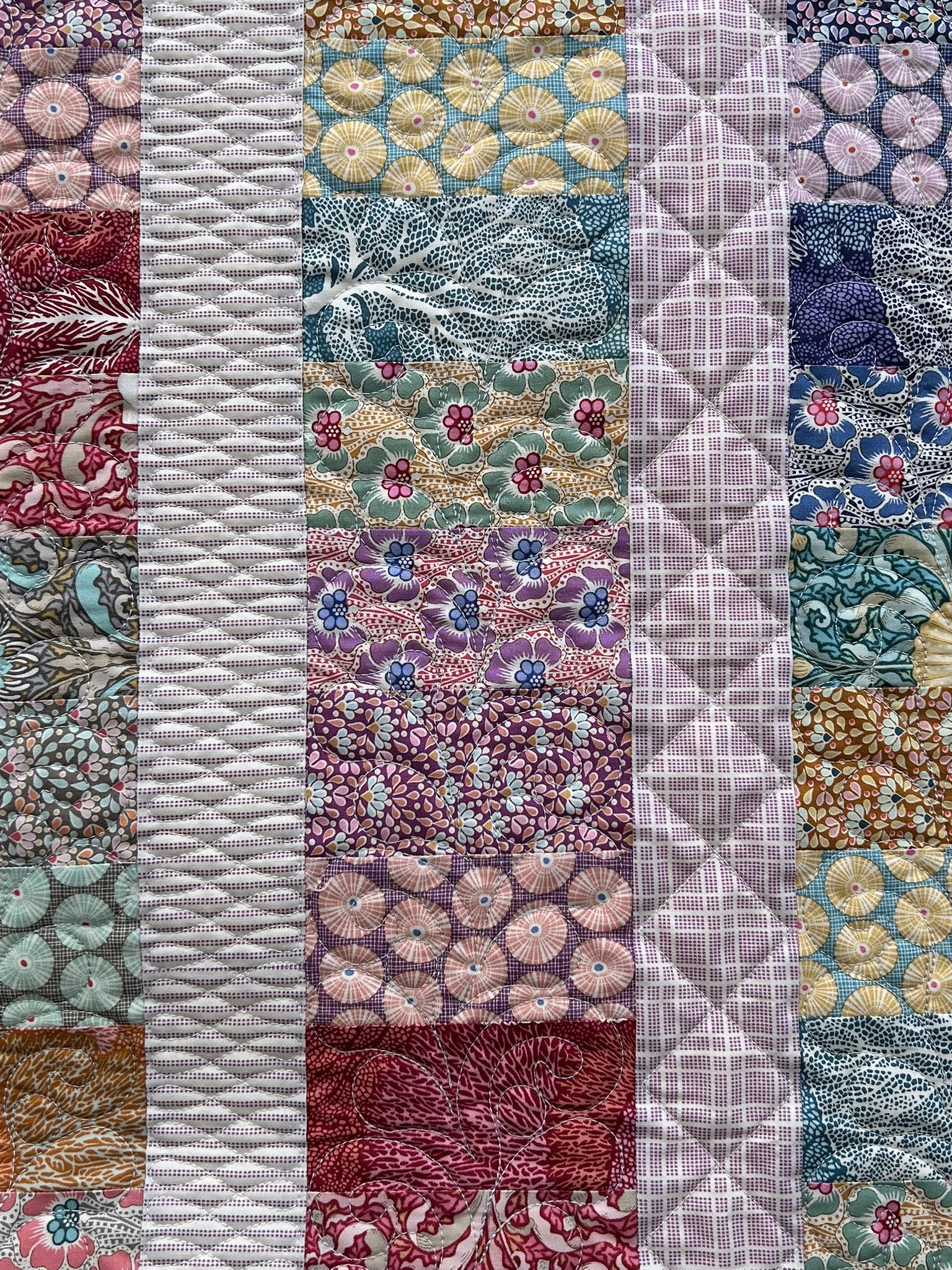 Close detail of the floral fabrics and varied geometric and flowing stitching on Libby’s Quilt