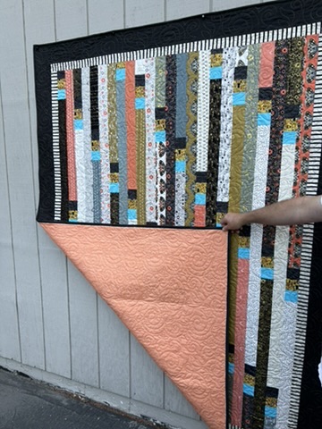 Folded view of Jelly Roll Race Quilt showing its warm coral reverse and quilted stitching
