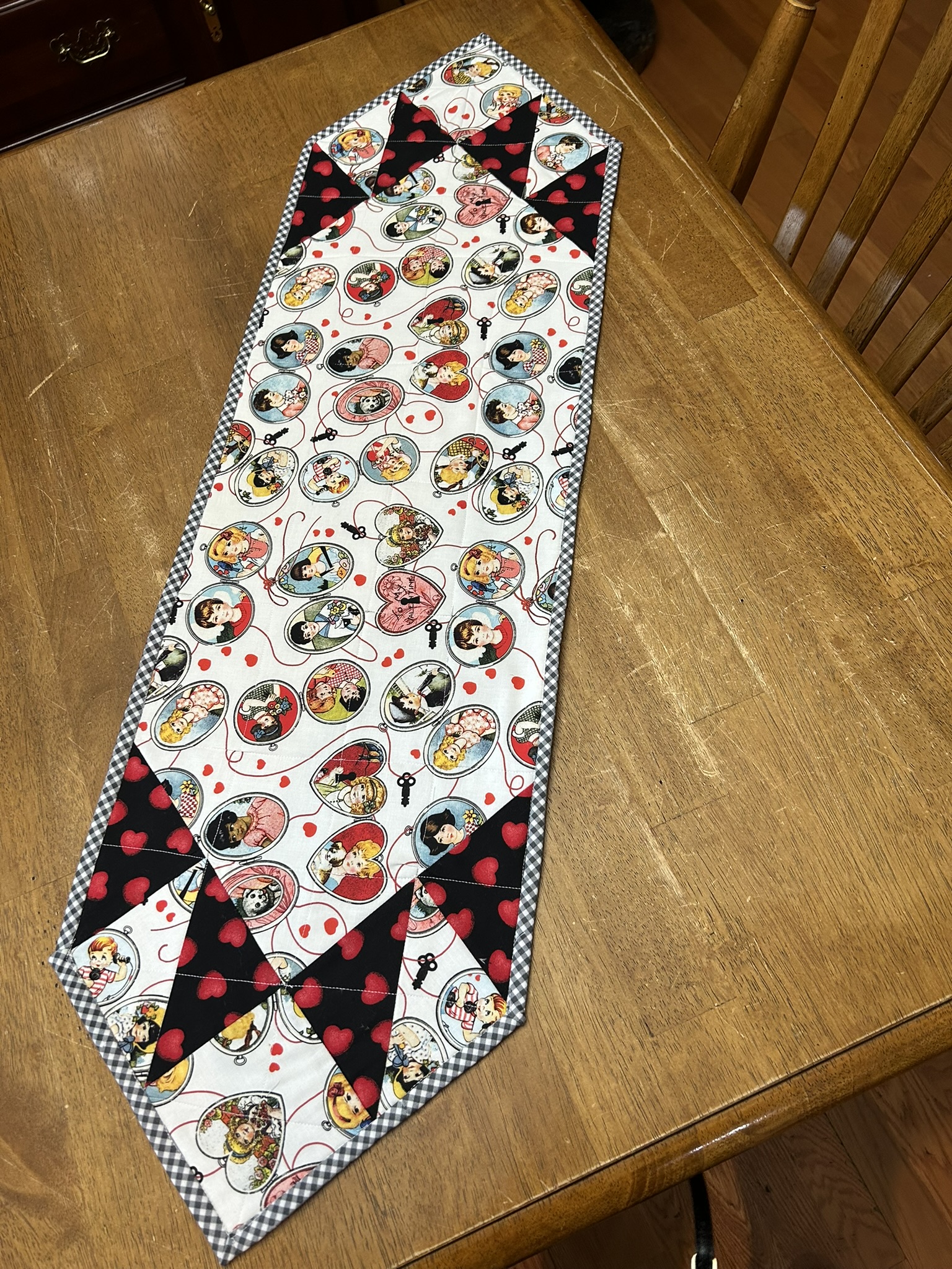 Front view of Barney’s Valentine’s Day Table Runner by Michele Urbany Neely Puluti with vintage Valentine portraits, red hearts, black pieced accents, and gingham binding