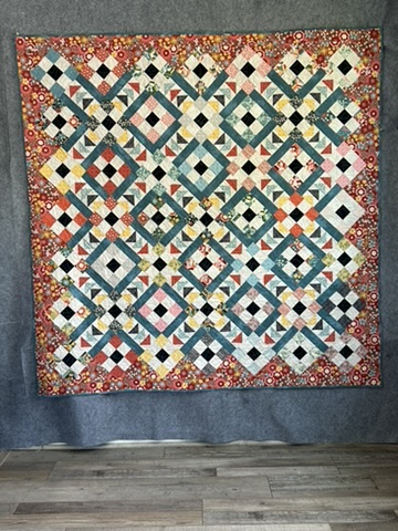 Basic Grey Modern Quilt by Michele Urbany Neely Puluti with interlocking teal, coral, cream, and black geometric lattice blocks and a rust floral border