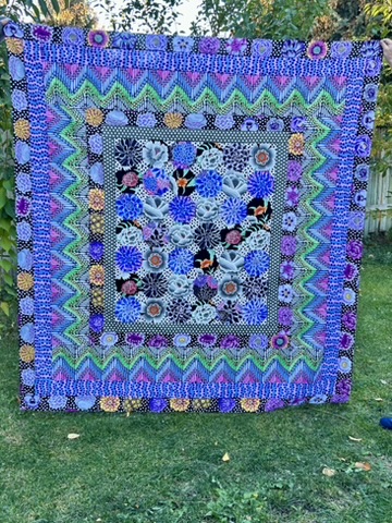 Full view of Michele Urbany Neely Puluti’s Snowball Quilt with layered blue, purple, turquoise, and green borders surrounding a floral center