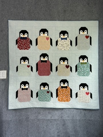 Penguins Baby Quilt by Michele Urbany Neely Puluti with twelve appliquéd penguins in patterned body panels on a pale blue quilted background