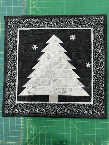 White Christmas tree wall hanging by Michele Urbany Neely Puluti on a black quilted background with snowflakes and a black-and-white patterned border