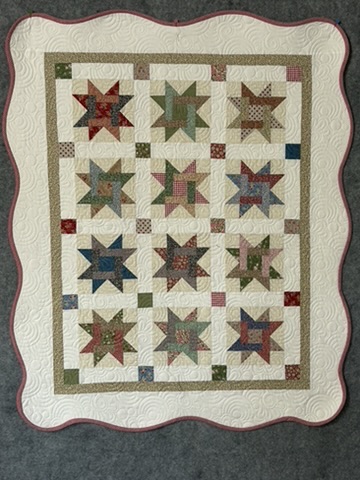 Tiny Stars Wall Hanging by Michele Urbany Neely Puluti, featuring twelve multicolored star blocks, cream quilting, and a softly scalloped border