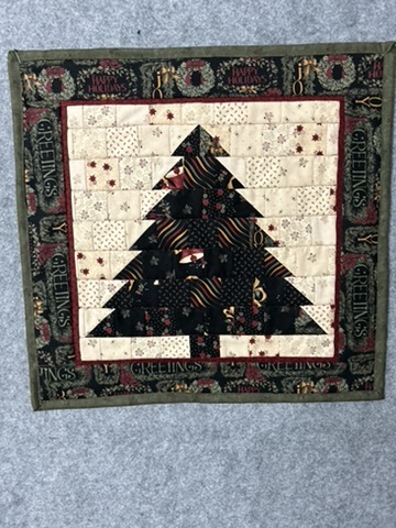Dark Christmas tree wall hanging by Michele Urbany Neely Puluti with colorful ribbon motifs, pale patchwork background, and holiday greetings border