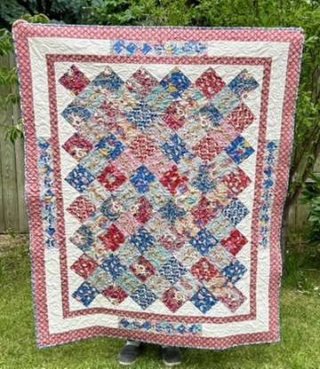 Full view of Ribbons Quilt by Michele Urbany Neely Puluti with interwoven diagonal floral bands in red, blue, cream, and teal framed by layered borders