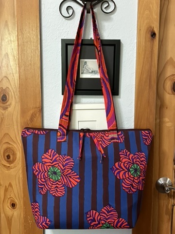 Exterior view of Tracy’s Purse by Michele Urbany Neely Puluti with blue and purple stripes, oversized red flowers, and long matching handles