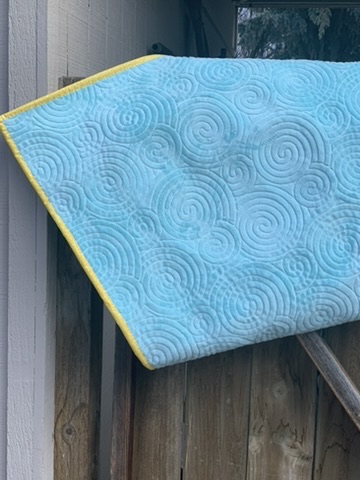 Reverse side of Hedgehog Baby Quilt showing blue fabric, spiral stitching, and yellow binding