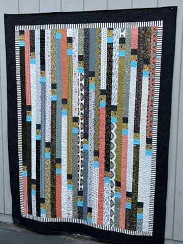 Full front view of Michele Urbany Neely Puluti’s Jelly Roll Race Quilt with vertical multicolored fabric strips and black border