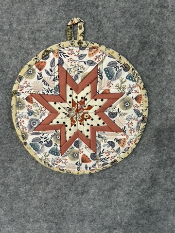Round Scrappy Potholder with a rust, cream, and black star over a botanical print